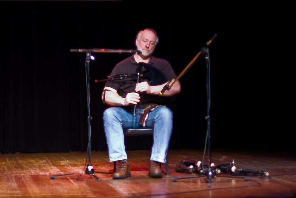 man seated in a chair playing a set of Scottish smallpipes
