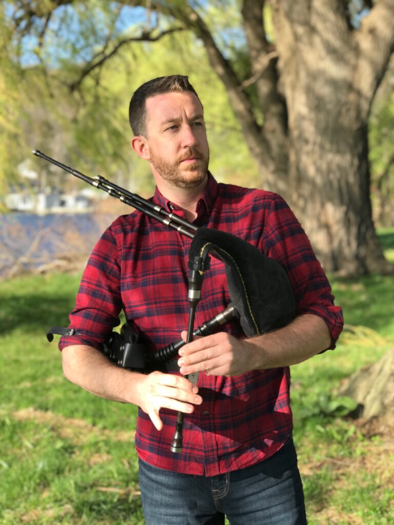 Michael Roddy man in red and black checked shirt outdoors holding Scottish smallpipes